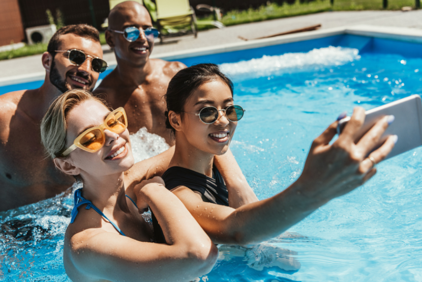 Two men and two women in a pool taking a selfie wearing sunglasses