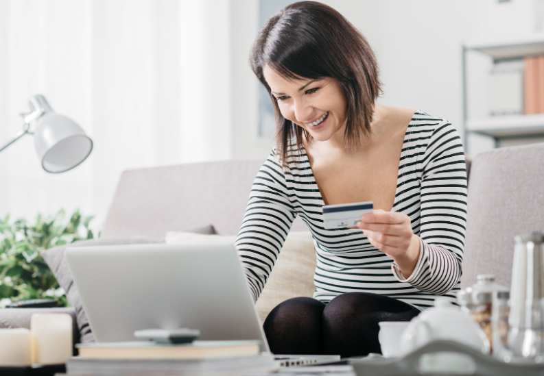 A woman smiling while on a laptop with a credit card in her hand