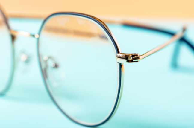 close up of side of round glasses with ultra thin lens on a light blue table 